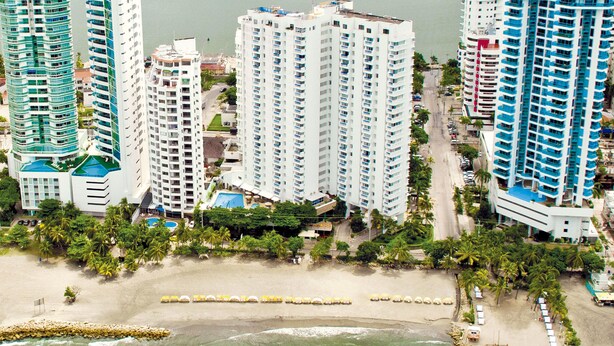 Ein Hochhaus-Hotel mit mehreren Etagen, ein Strand im Vordergrund und Blick auf den Ozean.