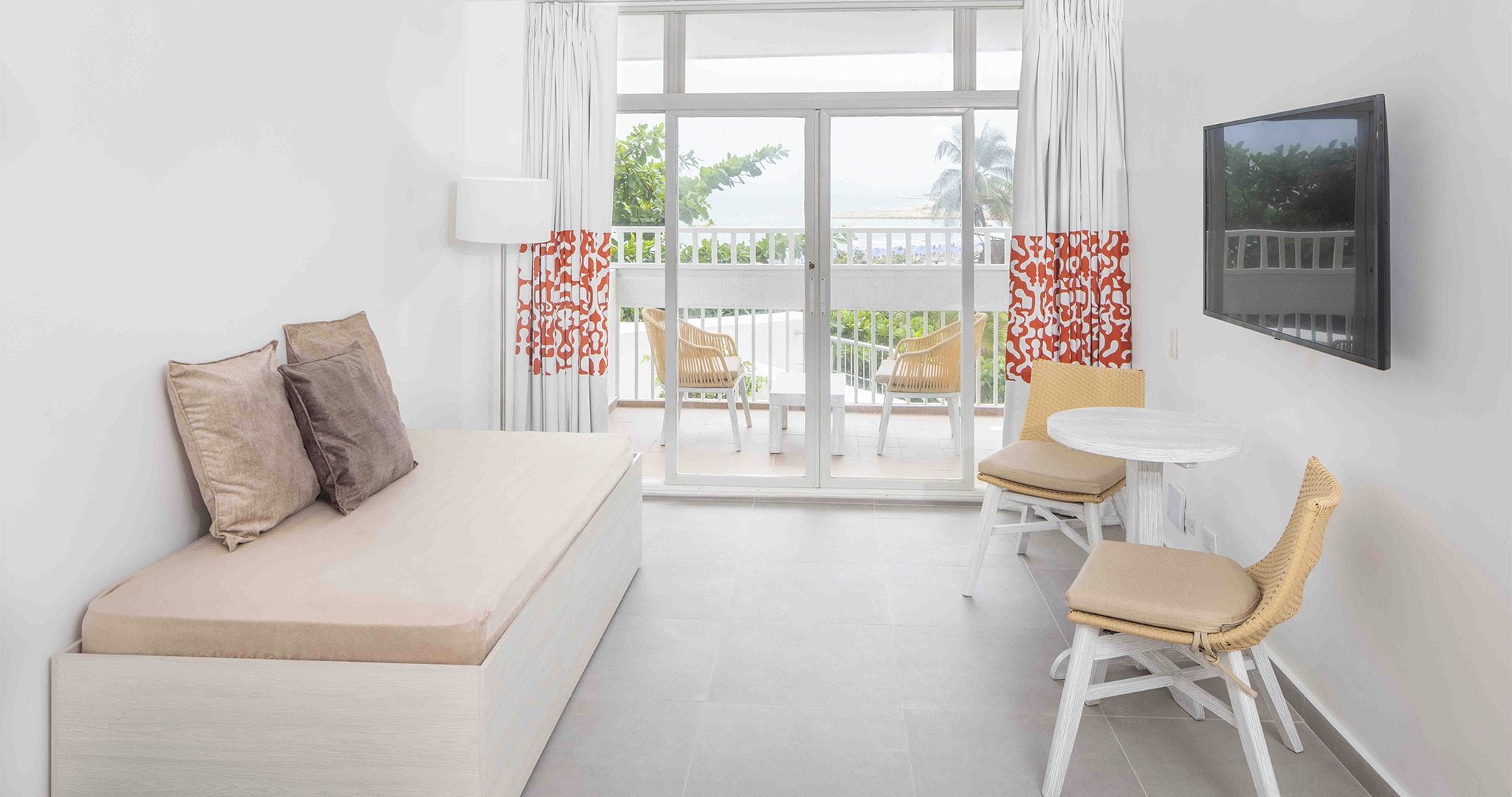 Quarto de hotel moderno com cama, uma mesinha, duas cadeiras e varanda com vista.