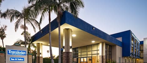 A Travelodge Inn & Suites with a blue exterior, palm trees, and a clear sky.