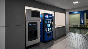 A vending machine and an ice dispenser in a hallway with tiled flooring and a balcony with a railing. - Travelodge Inn & Suites by Wyndham Anaheim on Disneyland Dr (Anaheim)