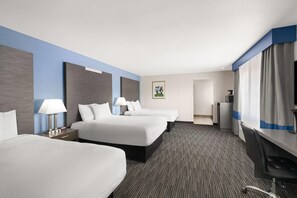 Habitación de hotel con tres camas, un escritorio y una silla.