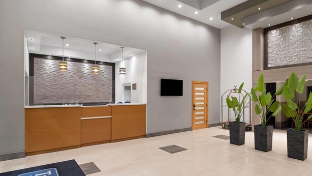 A modern reception area with a wooden counter, a flat-screen TV, and three potted plants. - Travelodge Inn & Suites by Wyndham Anaheim on Disneyland Dr (Anaheim)