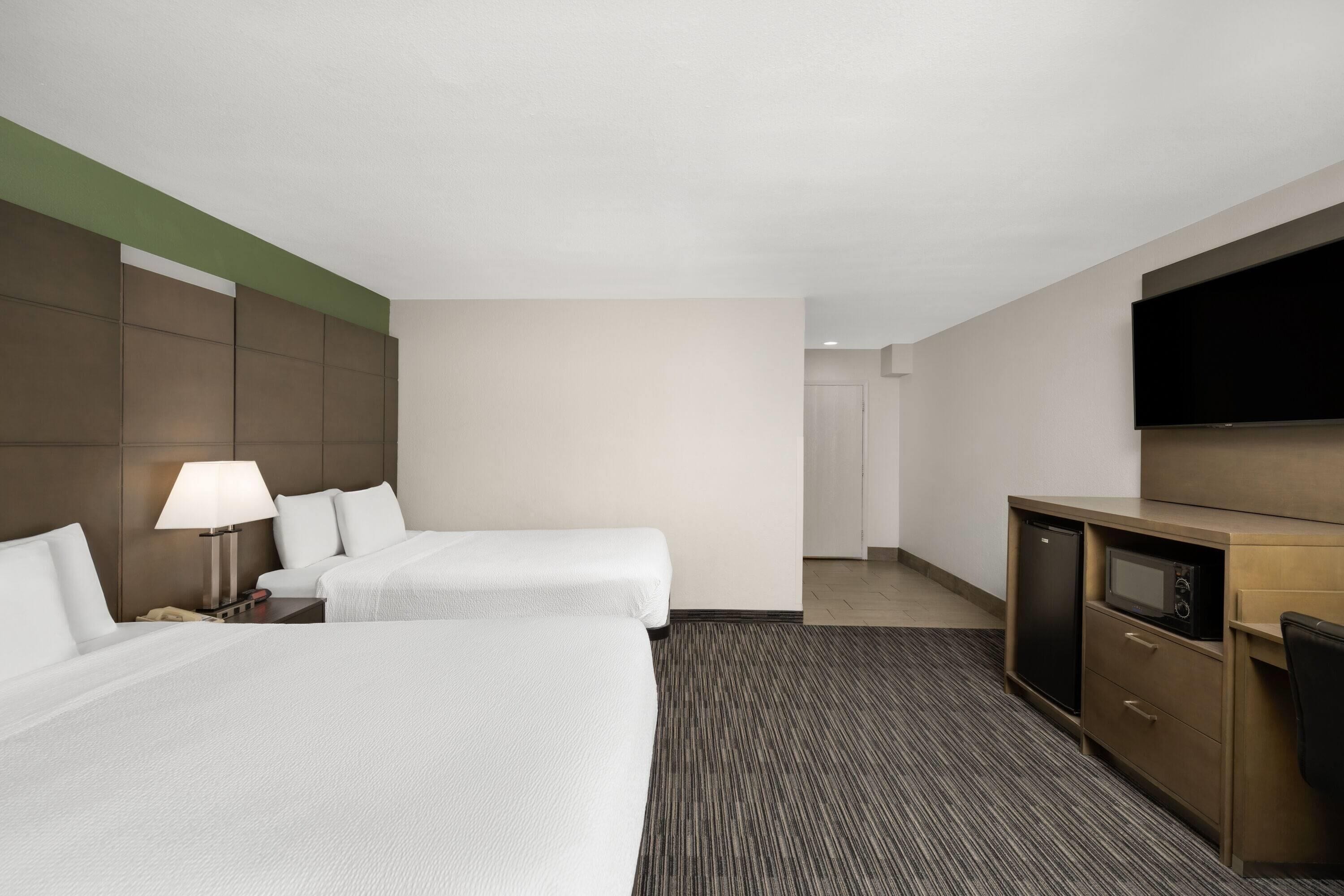 A hotel room with two beds, a desk with a flat-screen TV, a microwave, and a small refrigerator.