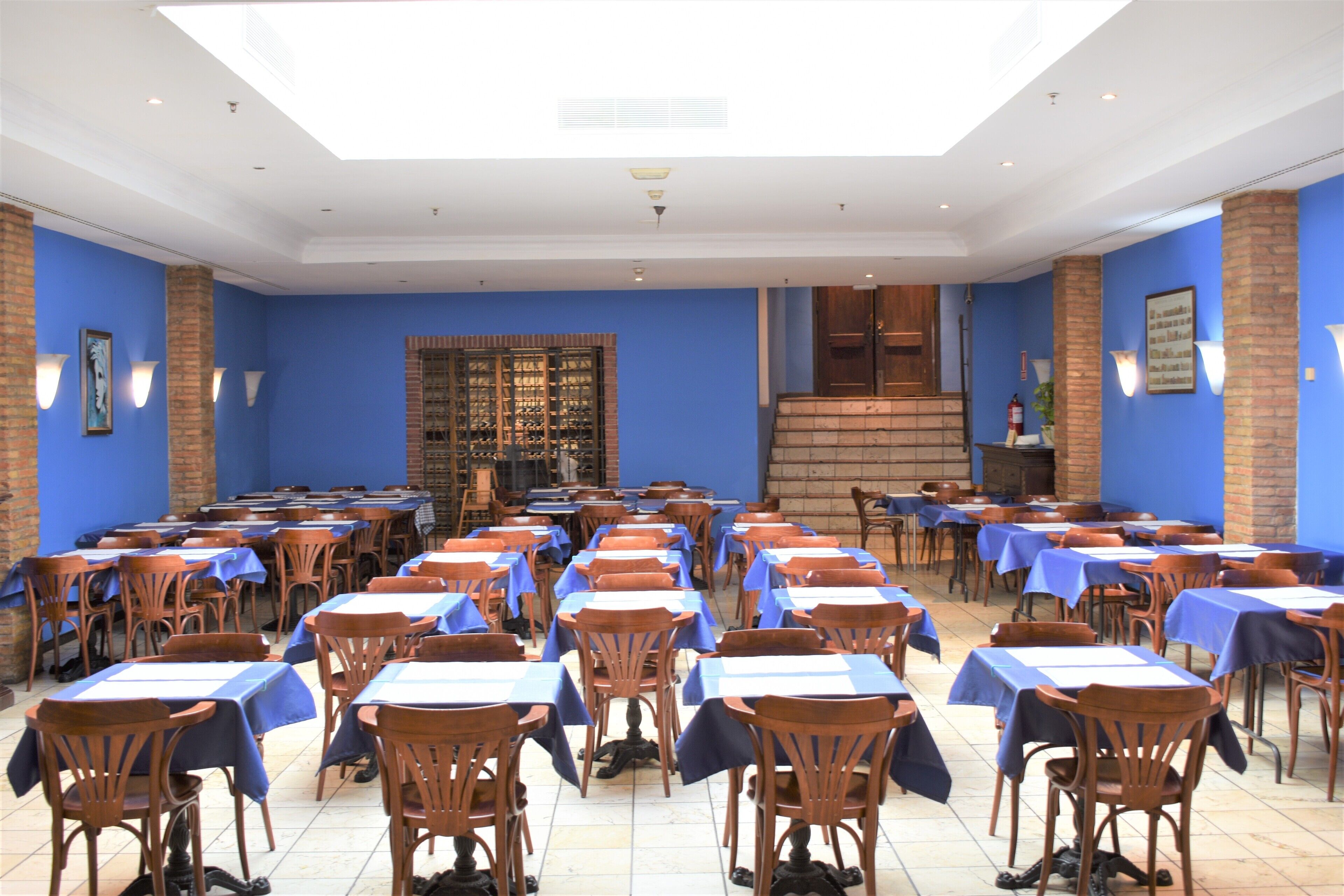 A large dining hall with rows of tables and chairs, a brick wall, and a skylight.