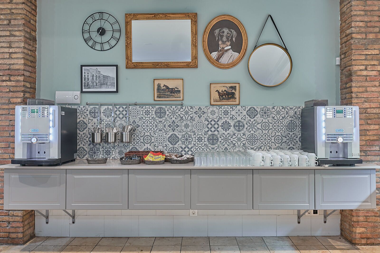 A coffee station with two Cino coffee machines, a clock, framed pictures, and a mirror on the wall.