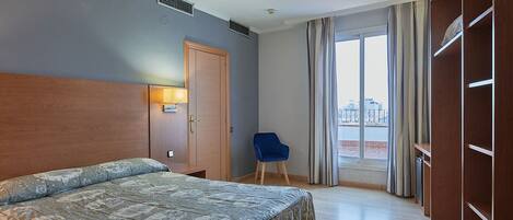 A hotel room with a bed, a wardrobe, a chair, and a view of the city through the window.