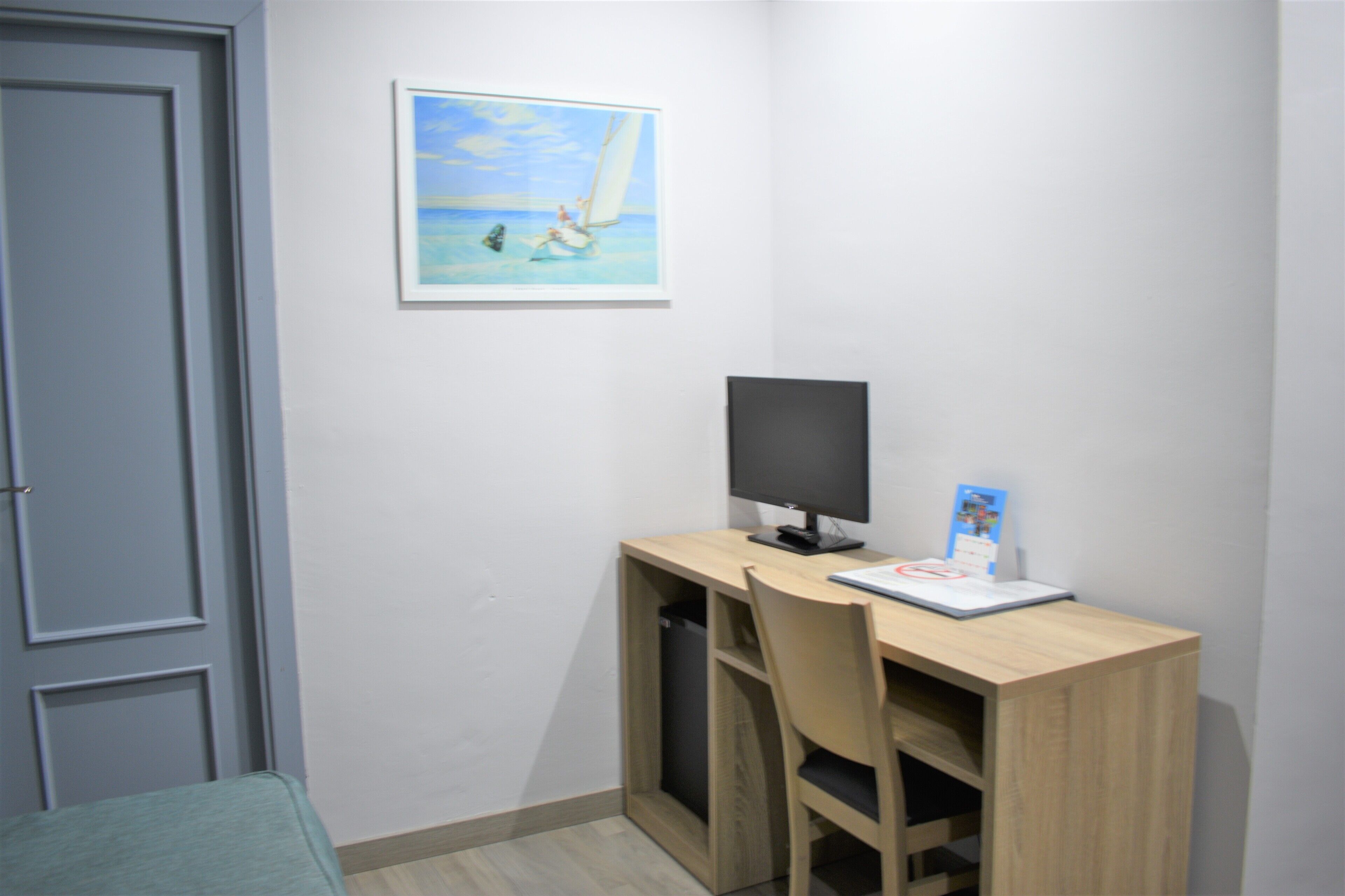 Quarto com escrivaninha, cadeira e quadro de um veleiro na parede.