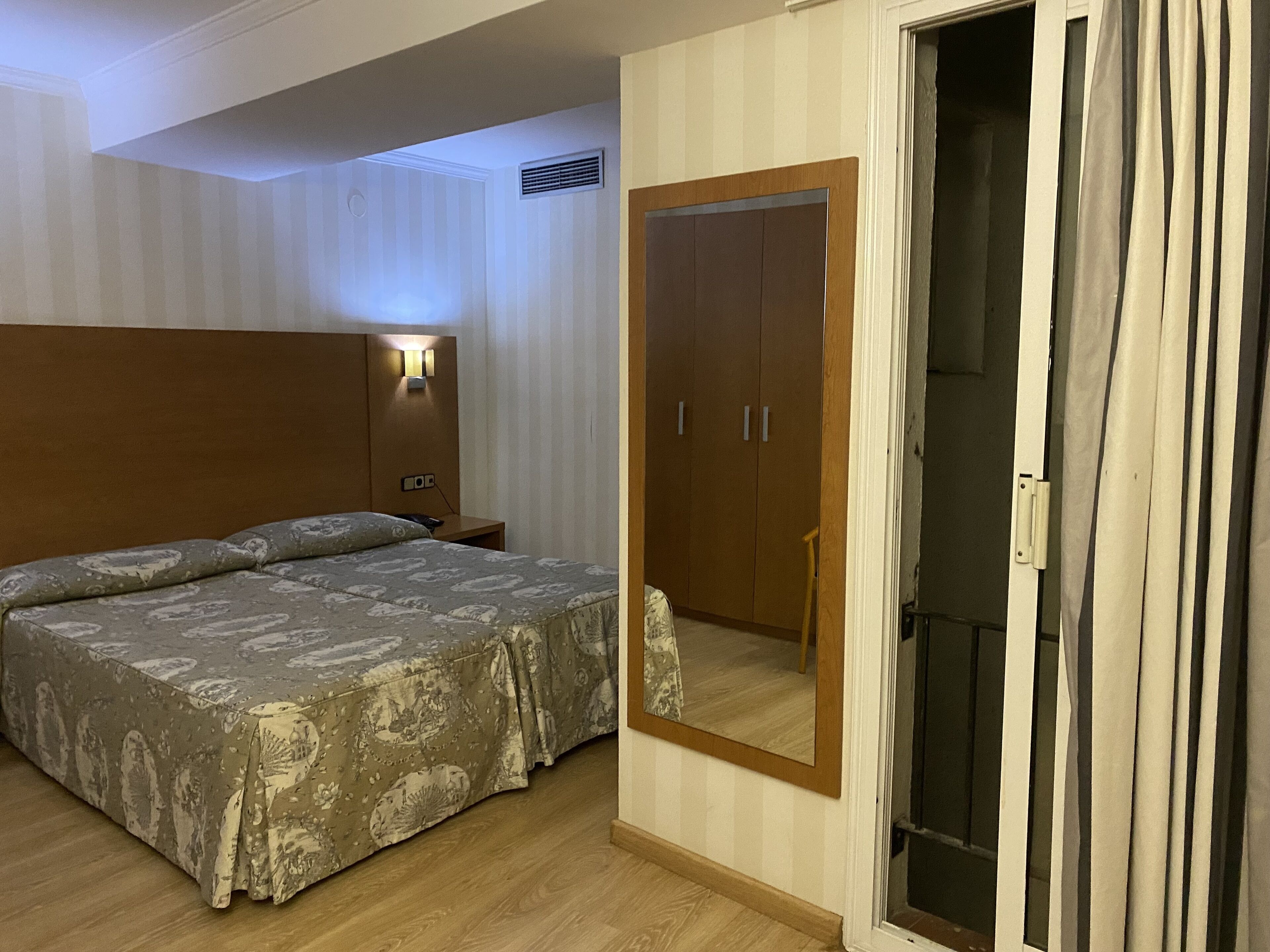 Una habitación de hotel con cama, armario, espejo y mesita de noche.
