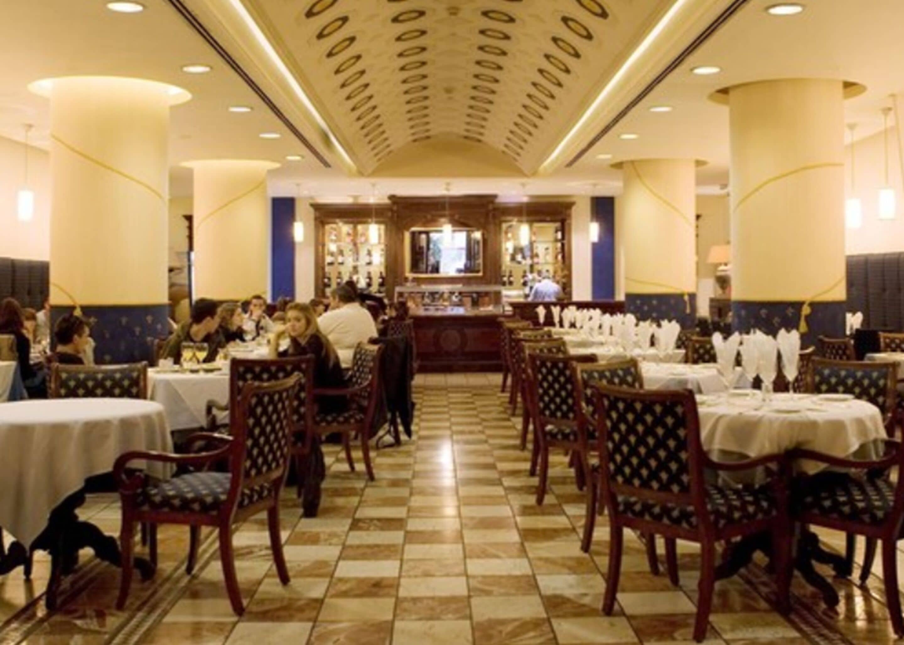 Un restaurante con suelo a cuadros, sillas de madera y mesas dispuestas para comer.