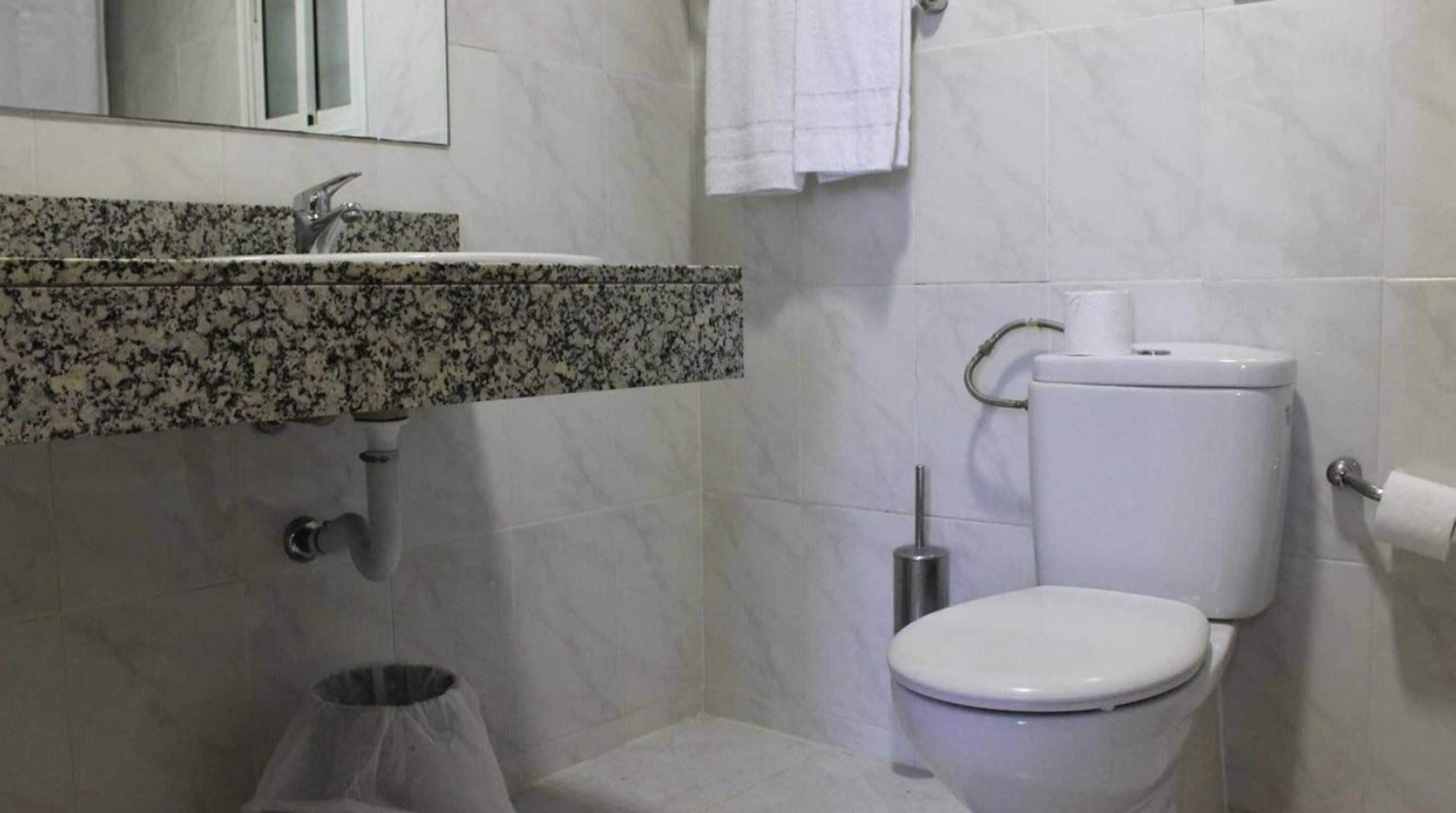 A bathroom with a granite countertop sink, a toilet, and a trash can.