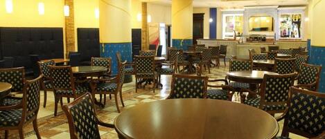 Un restaurant avec des tables rondes et des chaises à motifs, un sol carrelé et un bar situé au fond de la salle.