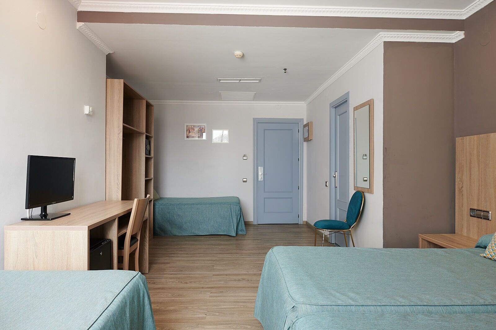 A hotel room with two beds, a desk with a computer, a chair, and a wardrobe.