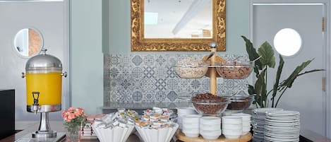 Disposição de buffet de café da manhã com dispensador de suco, jarras de café e diversas opções de alimentos.