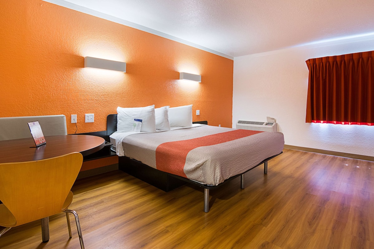 A hotel room with a bed, a desk, and a chair. There is a window with curtains.
