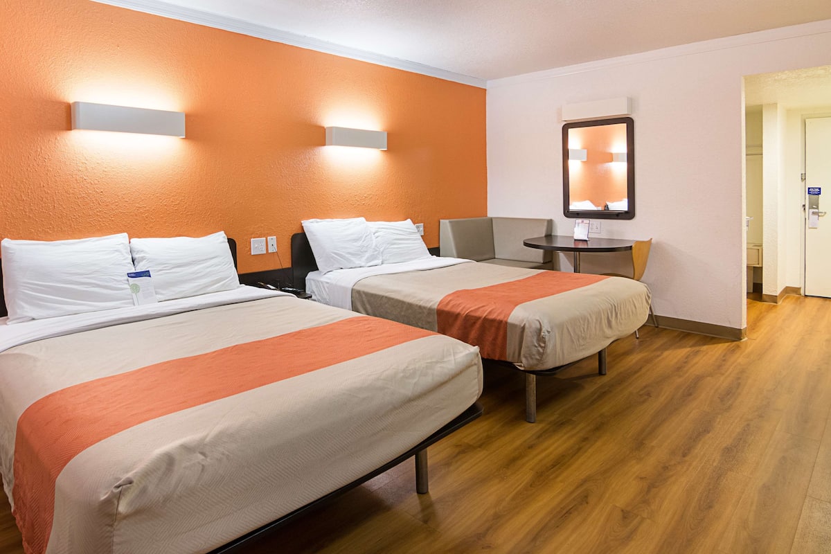 A hotel room with two beds, a small table, a chair, a mirror, and a door.