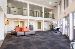 A spacious lobby with a high ceiling, a seating area with a sofa and chairs, a reception desk, and a large window offering a view of the outside. - Motel 6 Tampa, FL - Fairgrounds (Tampa)