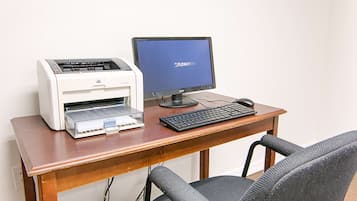 Uma mesa de madeira com uma impressora, um monitor de computador, um teclado e um rato.