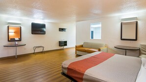Una habitación de hotel con una cama, un sofá, una mesita, un televisor y un espejo.