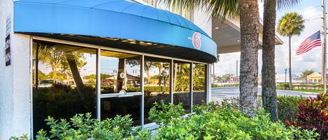 A motel with a blue awning, palm trees, and an American flag.