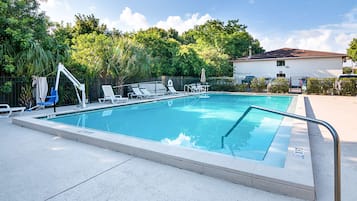 Una piscina rectangular con barandilla de seguridad metálica, rodeada de sillas de descanso y un área de estar cubierta.