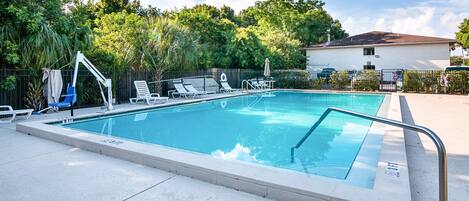 Una piscina rectangular con barandilla de seguridad metálica, rodeada de sillas de descanso y un área de estar cubierta.