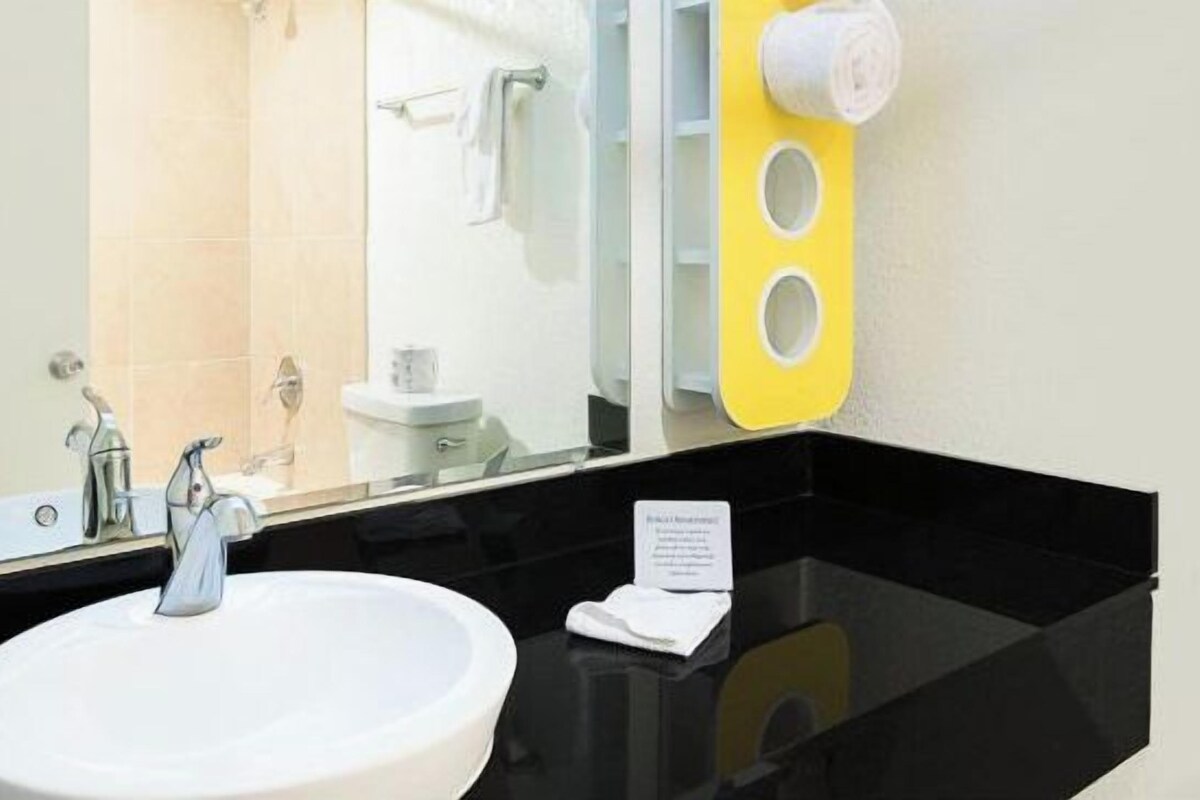 Une salle de bain avec un lavabo blanc, deux robinets, un miroir et un distributeur de serviettes jaunes.