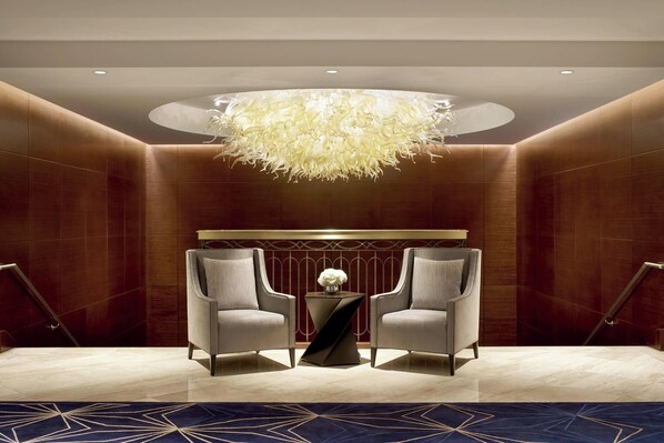A modern lobby with two armchairs, a central table, a decorative chandelier, and a patterned carpet.