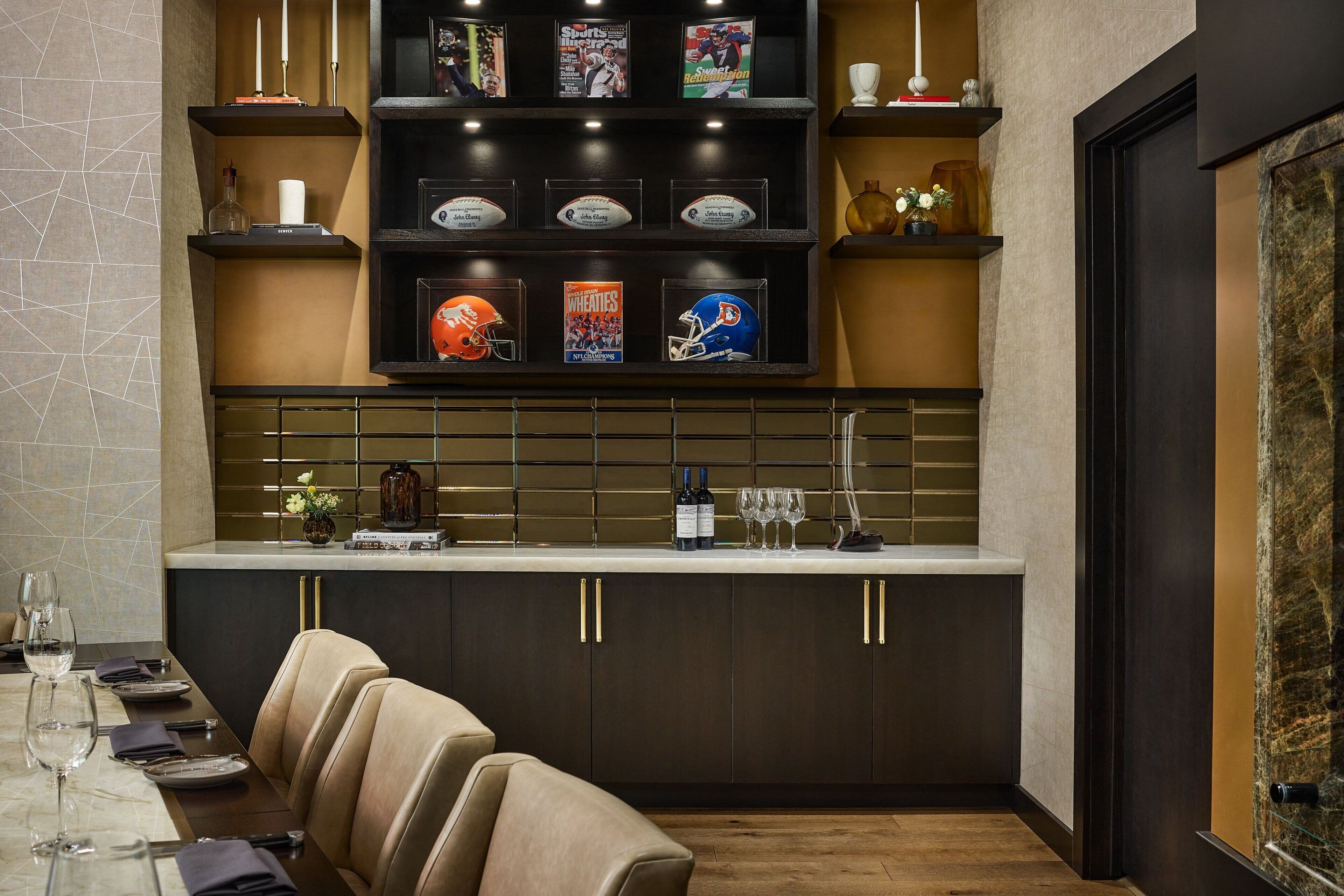 A modern kitchen with dark cabinetry, a marble countertop, and a dining area with leather chairs.
