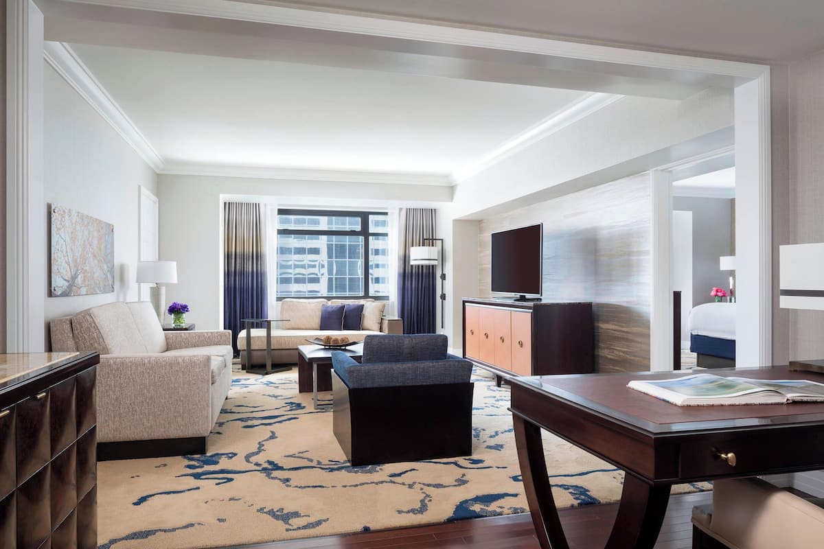 A modern hotel room with a sofa, a coffee table, a desk, and a television.