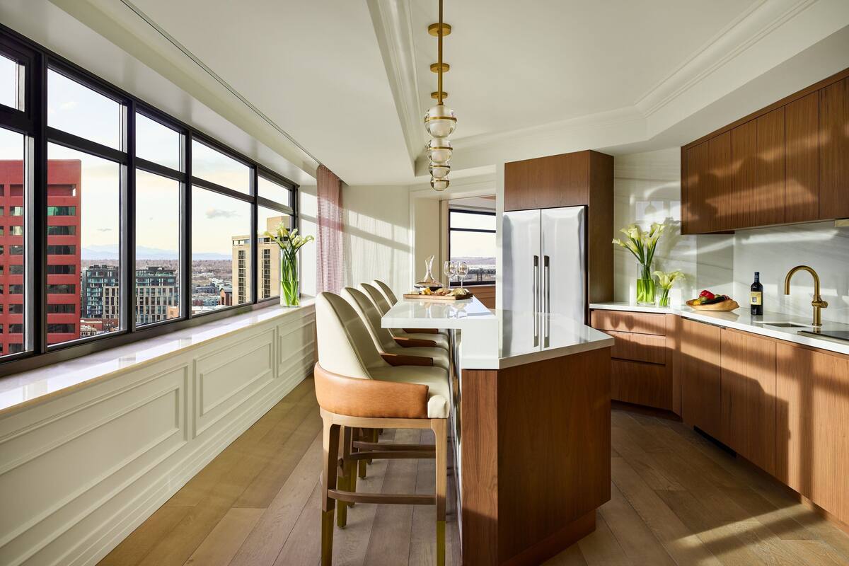 A modern kitchen with a large island, wooden cabinets, and a view of the city through large windows.