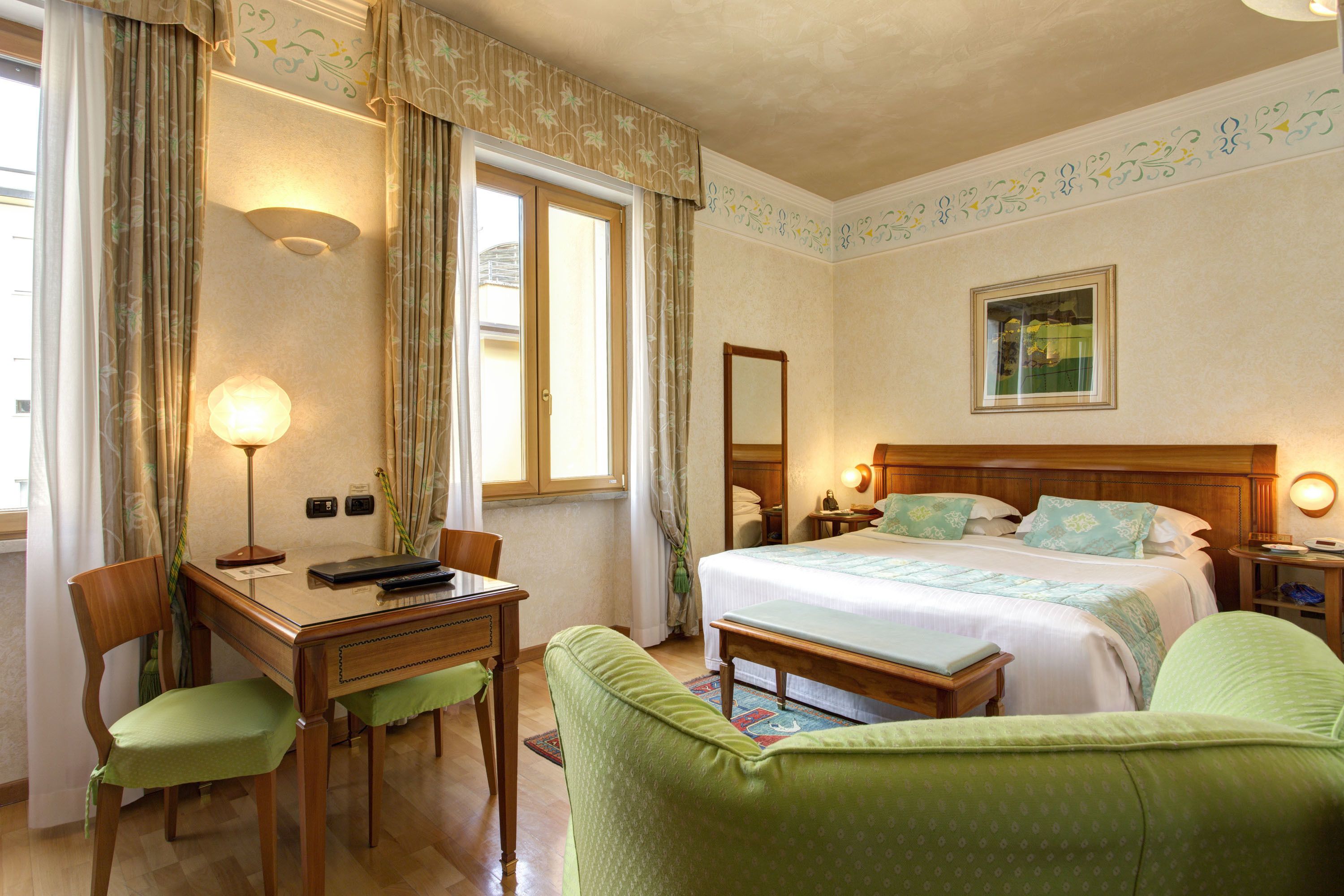 Ein Hotelzimmer mit Bett, Schreibtisch, Stuhl, Lampe und einem Bild an der Wand.