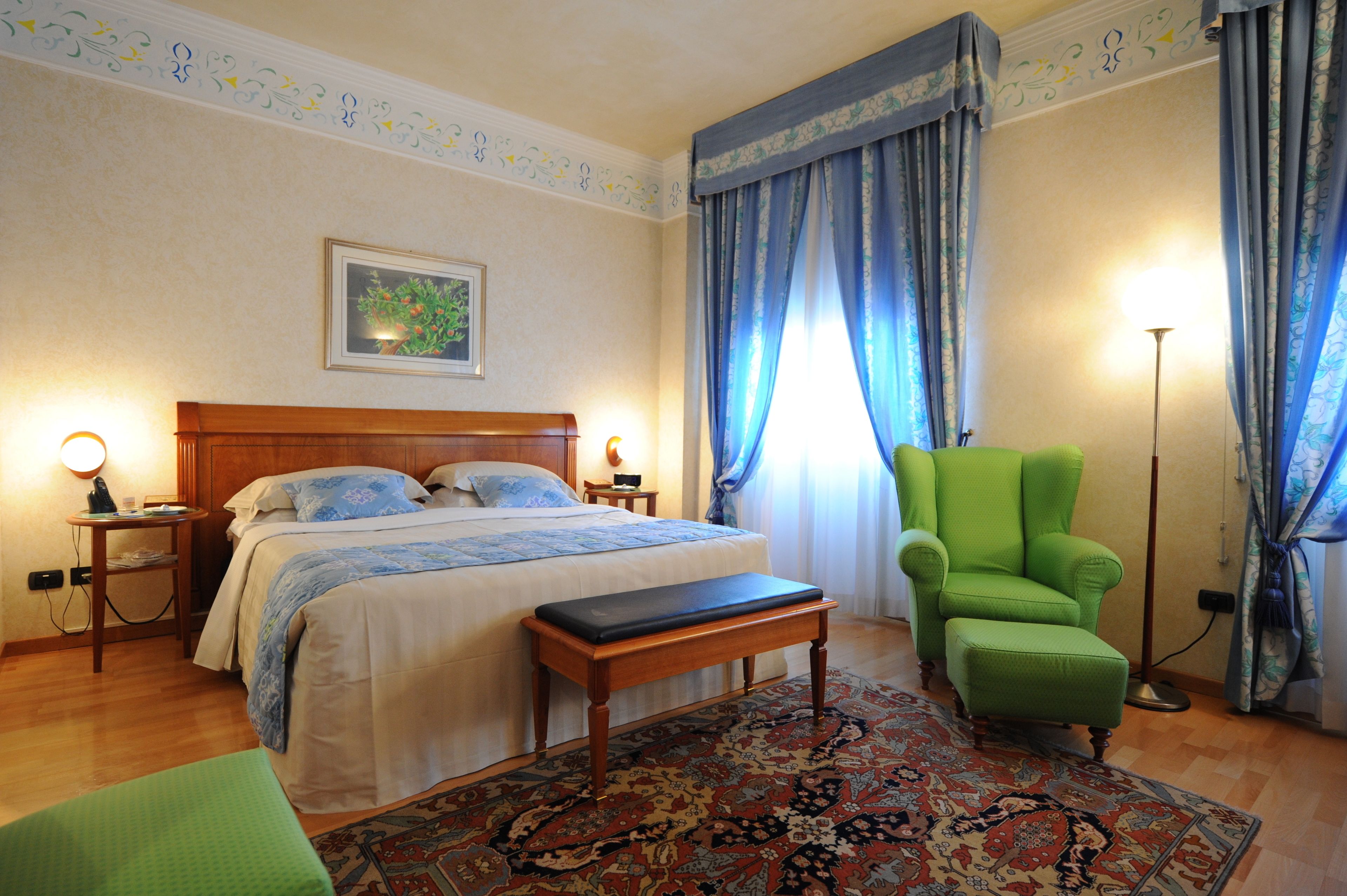 A bedroom with a bed, a bench, a chair, a bedside table, a floor lamp, and a patterned rug.