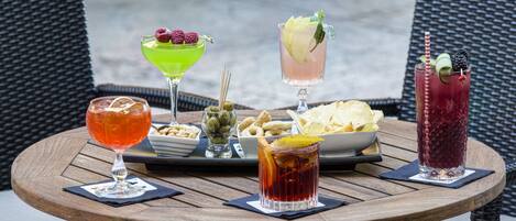 A round wooden table with four drinks and a snack tray.