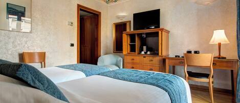 A hotel room with two beds, a desk, a chair, a television, and a lamp.