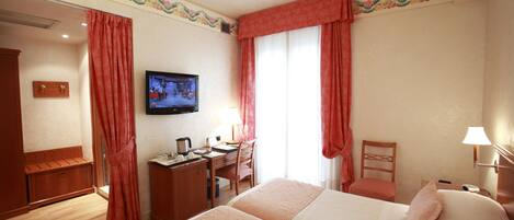 Habitación de hotel con dos camas, un escritorio, una silla, un televisor y una ventana con cortinas.
