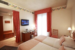 Habitación de hotel con dos camas, un escritorio, una silla, un televisor y una ventana con cortinas.