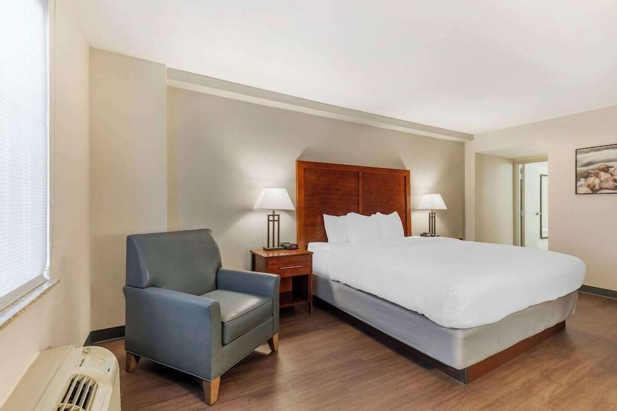 A hotel room with a bed, a chair, two bedside tables with lamps, a heater, and a mirror on the wall.