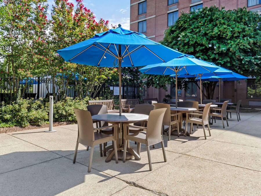 Outdoor patio seating with round tables and chairs, blue umbrellas, and a brick building in the background.