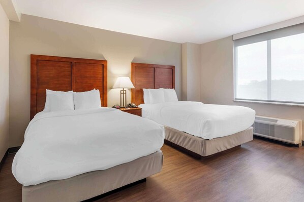 Habitación de hotel con dos camas, una mesita de noche con lámpara y un ventanal grande con persianas.