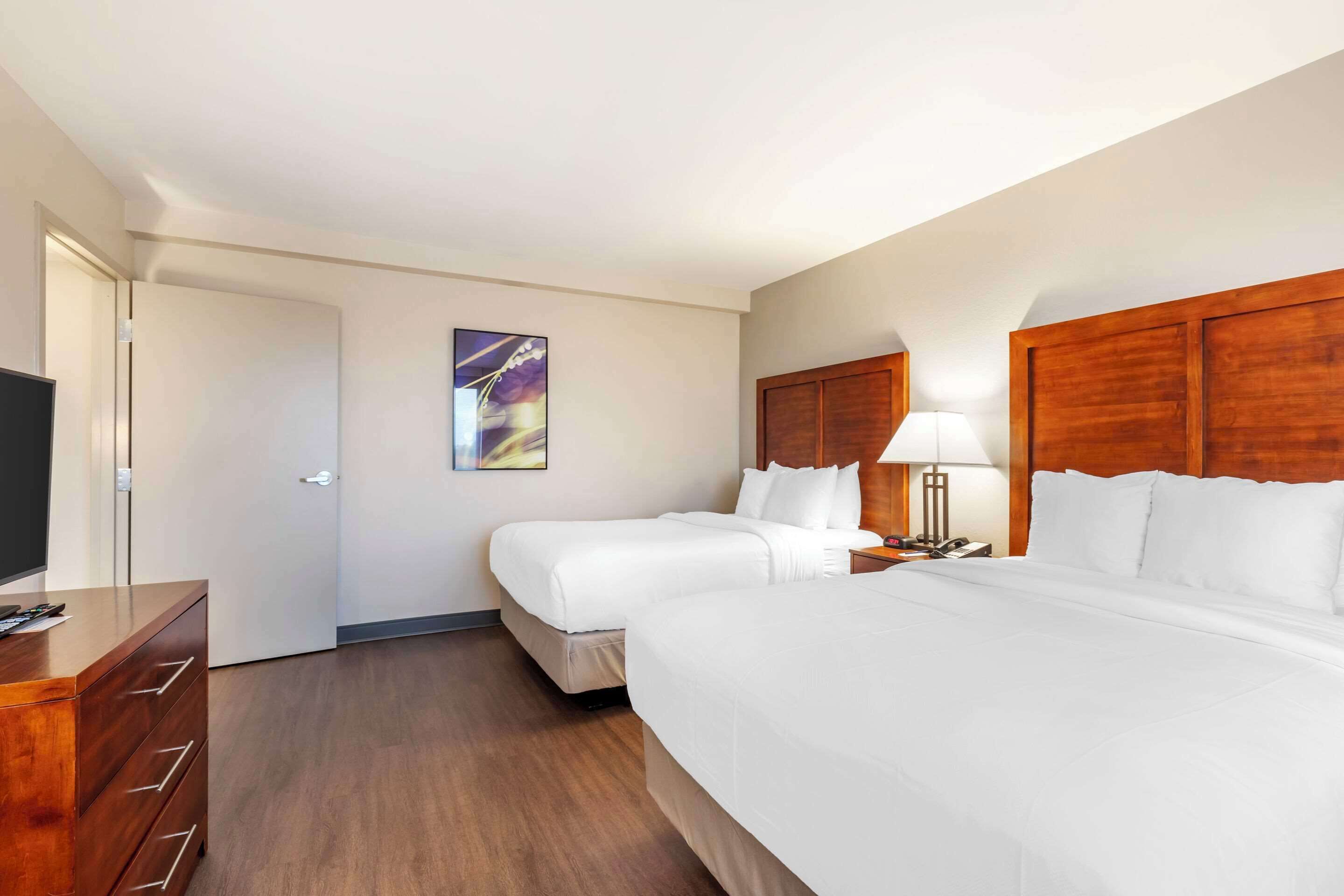 Habitación de hotel con dos camas, un aparador de madera, un televisor y un cuadro en la pared.