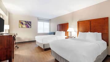 A hotel room with two beds, a desk, a chair, a TV, a window, and a painting on the wall.