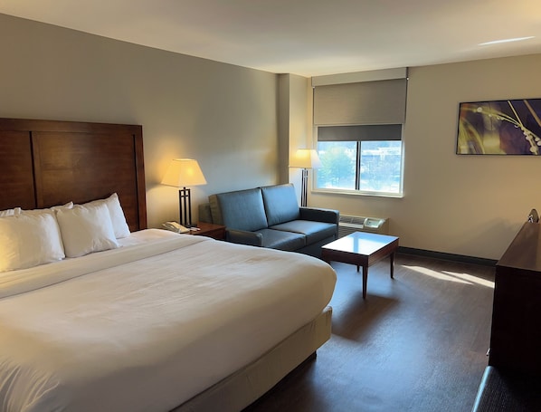 A hotel room with a large bed, a sofa, a small table, and a window with a view.