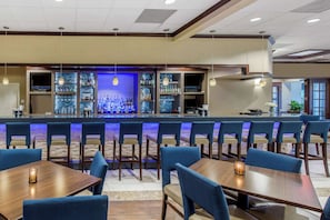 A bar area with multiple seating options, including bar stools and tables, and a variety of bottles and glasses on shelves.