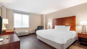Une chambre d’hôtel avec un grand lit, deux tables de chevet avec des lampes, un bureau avec une lampe, une chaise et une fenêtre avec des stores.