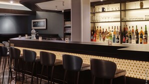 A bar area with a patterned light feature, a selection of liquor bottles, and bar stools. - Dorint Hotel Würzburg (Würzburg)