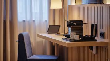 Ein modernes Hotelzimmer mit Schreibtisch, Laptop, Kaffeemaschine und einem Sessel.