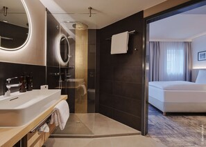 A modern hotel bathroom with a large mirror, a glass-enclosed shower, a bathtub, and a toilet. - Dorint Hotel Würzburg (Würzburg)