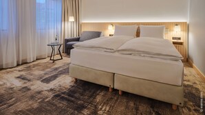 A hotel room with a large bed, a chair, a small table, and a lamp. - Dorint Hotel Würzburg (Würzburg)