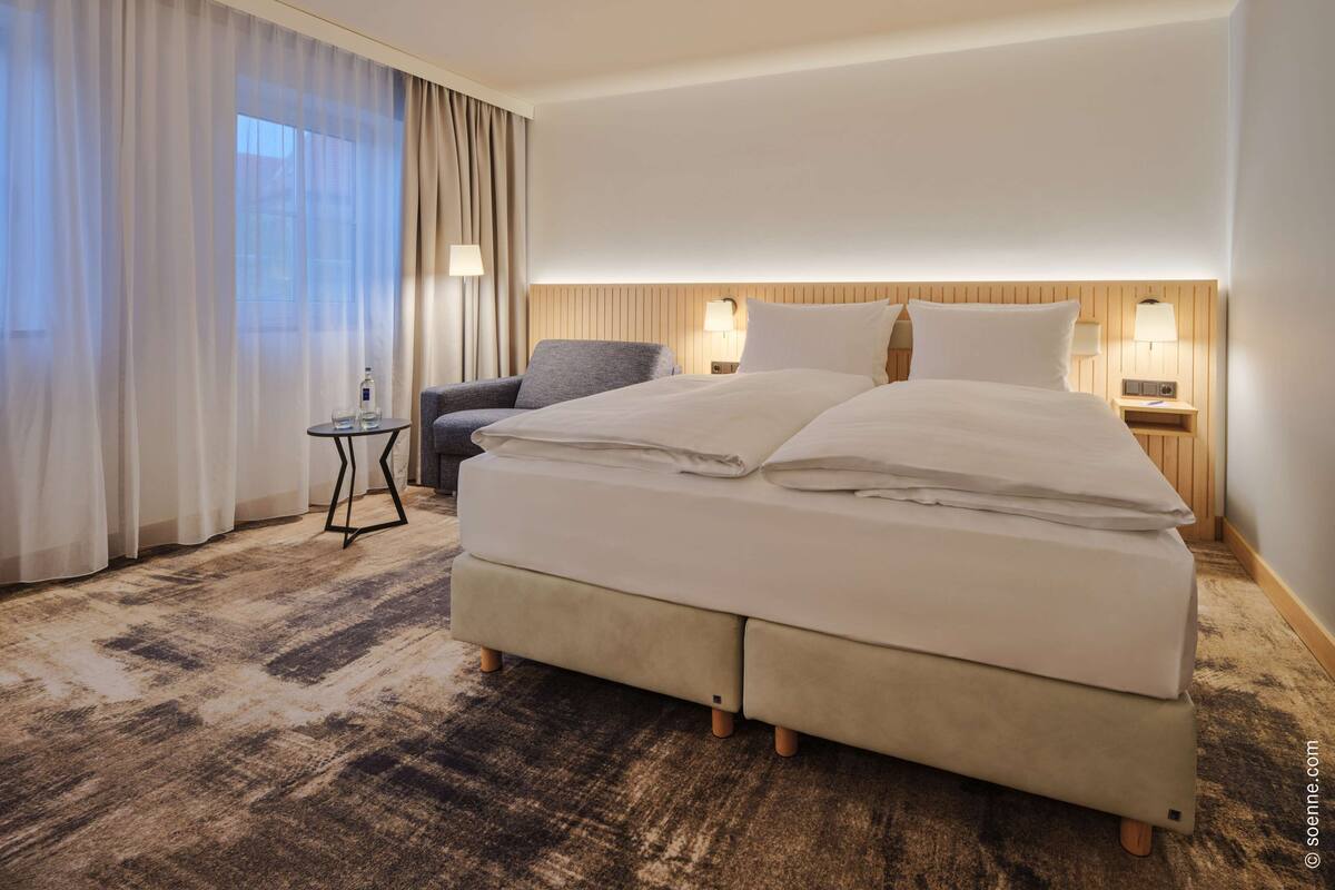 A hotel room with a large bed, a chair, a small table, and a lamp.