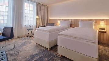 A hotel room with two beds, a desk, a chair, and a view of the outside through large windows.